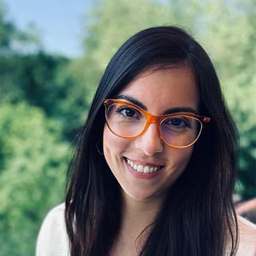 Eine lächelnde Frau mit Brille vor einem grünen Hintergrund mit Bäumen