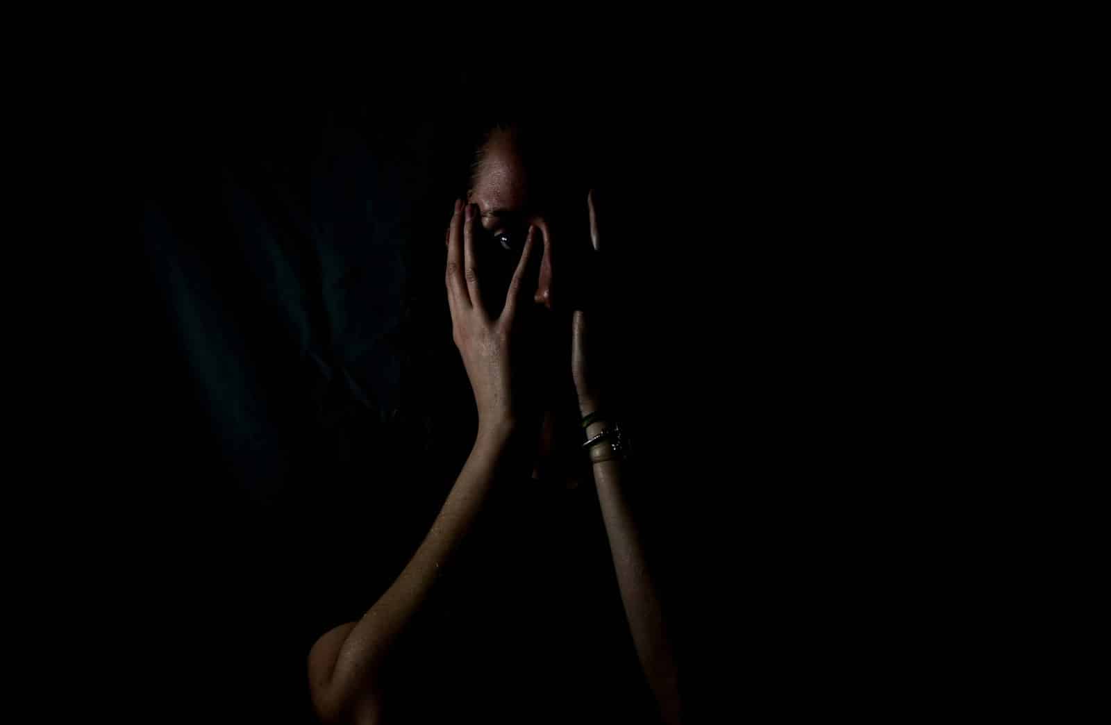 Eine Frau umgeben von Dunkelheit, die sich die Hände vor das Gesicht hält